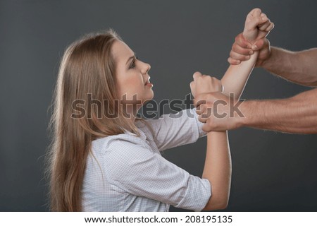 Man holding hands of very scared fair-haired woman. Isolated on grey background