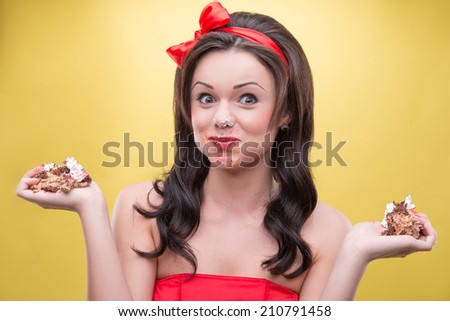 Half-length portrait of happy slovenly dark-haired woman wearing great red headband holding two pieces of her favorite dessert in both hands satisfied with her life. Isolated on yellow background