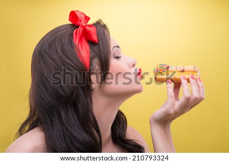 Very beautiful dark-haired woman wearing nice red headband with closed eyes wanted to kiss her favorite sweets. Isolated on yellow background
