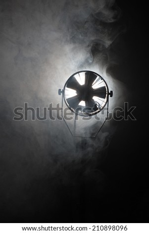 Switched cinema spotlight standing in the dark enveloped in smoke