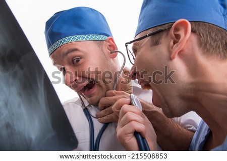 Half-length portrait of two doctors wearing blue caps one of them keeping a stethoscope and another shouting something in it holding the radiograph. Isolated on white background