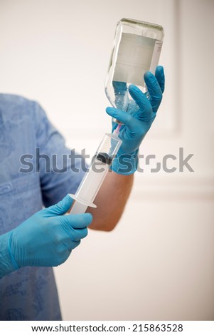 Selective focus on the surgeon wearing blue disposable gloves filling a syringe with fluid