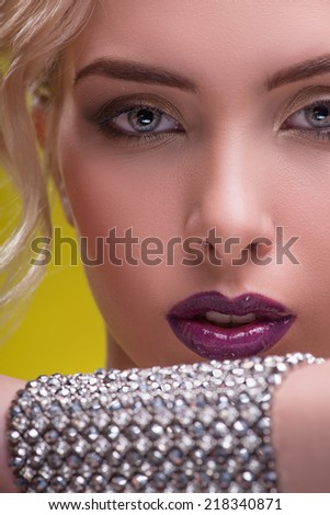 Half-length portrait of beautiful sexy blonde with violet tempting lips and perfect skin showing us her precious bracelet isolated on yellow background. Close up