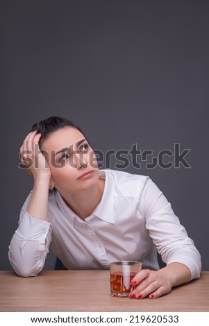 Half-length portrait of dark-haired beautiful woman wearing white blouse sitting at the table with the glass of beer thinking how to change her life. Isolated on dark background