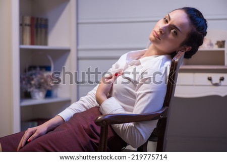 sapless woman wearing white blouse and vinous skirt sitting in the chair looking at us with despair in her eyes. Her office on background
