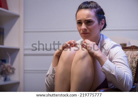 woman wearing white blouse sitting in the chair flexing her legs and thinking how to solve her problems. Her office on background