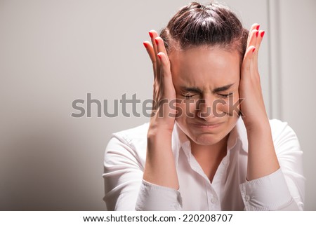 Half-length portrait of beautiful dark-haired young sad woman wearing white blouse and vinous skirt leaning on the table holding at her head crying driving into the corner