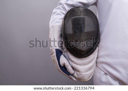 Half-length portrait of the girl wearing white fencing costume holding the fencing mask. Isolated on grey background