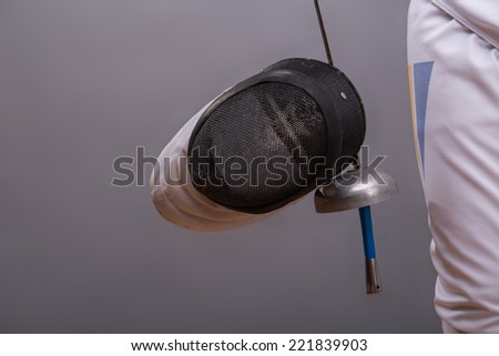 Portrait of the fencing mask which is hanging on the rapier in the hands of the fencer