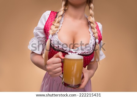 Half-length portrait of young sexy blonde with big breast wearing pink dirndl with white blouse holding the beer mug Isolated on dark background