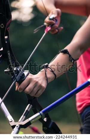 Selective focus on the bow which is pulled at something by lovely young fair-haired woman standing aside wearing pink T-shirt