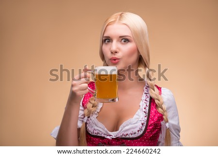 Young sexy blonde wearing pink dirndl with white blouse standing with beer mag taking pleasure in her favorite drink. Isolated on dark background