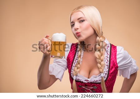 Half-length portrait of young sexy blonde standing aside wearing pink dirndl with white blouse adoring beer. Isolated on dark background