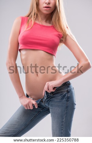 Half-length portrait of sexy beautiful blonde with great figure wearing pink vest and jeans showing us her tempting belly. Isolated on white background