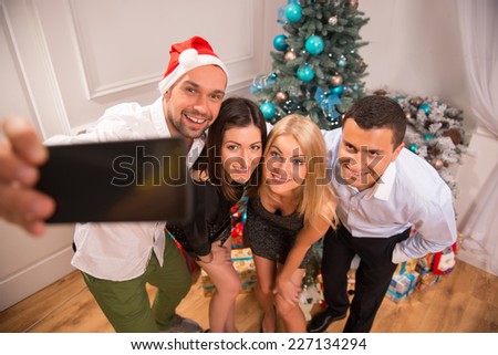 Half-length portrait of the happy smiling company of friends standing near the decorated New Year tree making photo having fun