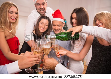 Half-length portrait of the company of happy young friends standing in a circle pouring the champagne greeting each other with the New Year