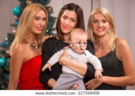 Half-length portrait of the dark-haired pretty smiling woman holding her little cute baby standing between two her best friends