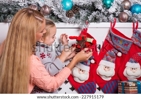 Half-length portrait of mom and little daughter taking out a pretty toy from the red Christmas socks