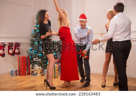Full-length portrait of the company of happy friends wearing great costumes dancing near the Christmas tree celebrating New Year drinking champagne