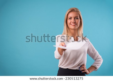 Half-length portrait of beautiful business lady wearing white classic blouse standing giving us the white sheet of paper for copy place. Isolated on blue background