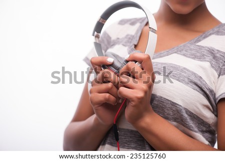 Selective focus on the lovely white earphones in the hands of smiling African girl wearing striped T-shirt