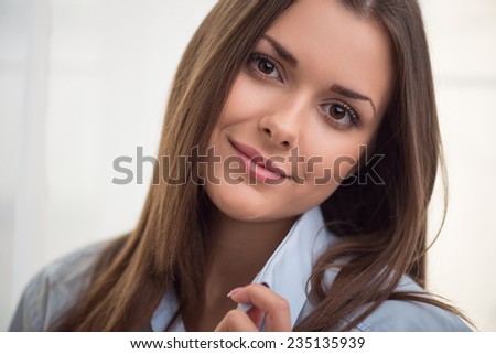 Half-length portrait of dark-haired beautiful smiling girl wearing blue shirt touching it looking at us waking up in the morning