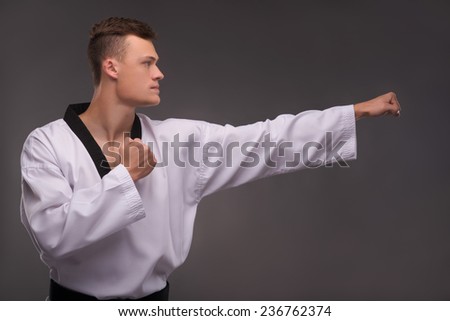 Half-length portrait of young handsome fair-haired karate enthusiast wearing white kimono standing aside training himself before the important fight. Isolated on the dark background
