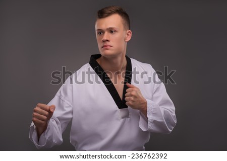 Half-length portrait of young handsome fair-haired karate enthusiast wearing white kimono coaching himself before the important fight. Isolated on the dark background