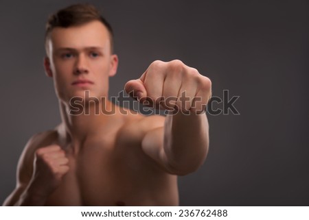 Selective focus on the fist of young handsome fair-haired bare-chested karate enthusiast coaching himself before the important fight