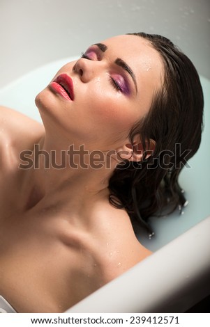 Half-length portrait of beautiful sexy dark-haired woman lying in the bath with closed eyes enjoying this moment and relaxing