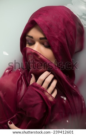 Half-length portrait of beautiful sexy dark-haired woman closing her eyes lying in the bath covering herself with the wine-colored cloth looking dreaming about something