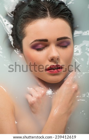 Half-length portrait of beautiful sexy dark-haired woman lying in the bath with closed eyes thinking about something enjoying this moment. Top view