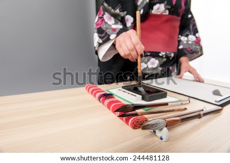 Japanese calligraphy. Low angle image of woman in kimono practicing calligraphy with brushes on paper placed on wooden table