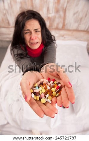 Sneezing woman. Top view image of young sick woman sneezing while sitting on bed with pills and tissues against wooden wall
