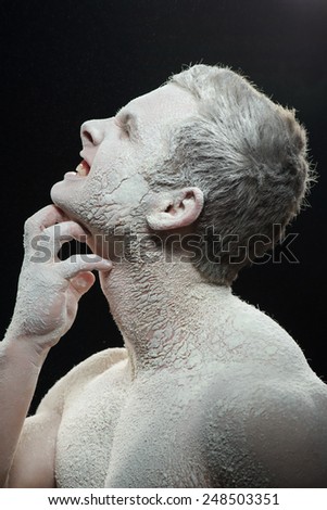 Suffering from itchy skin. Conceptual closeup portrait of angry shirtless man scratching his face and neck while covered with white powder on dark background