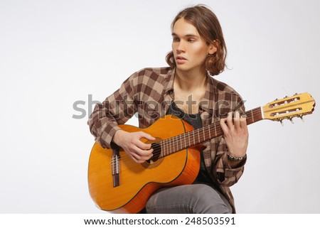 Creative soul. Handsome young guitar player playing acoustic guitar while sitting against white background