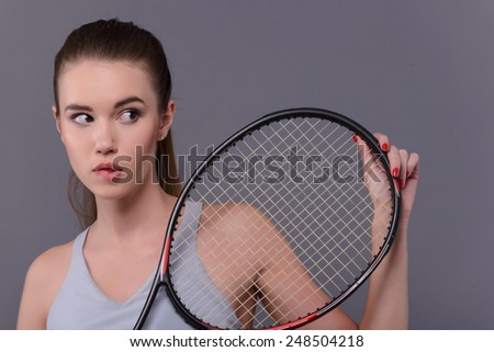 Not sure of victory. Closeup portrait of beautiful young woman in sports clothes holding tennis racket and biting lips while standing against white background with copy space