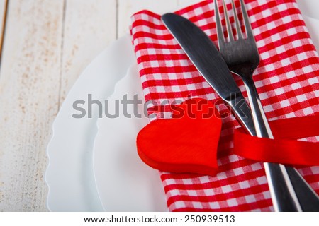The perfect romantic dinner. Closeup of wooden table served with romantic heart shape decor and cutlery on checkered napkin