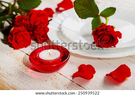 The perfect romantic dinner. Closeup of wooden table served with romantic red candle, white plate and beautiful roses