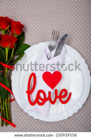 Serving up a little romance. Top view closeup of romantic dinner cutlery with red heart, love lettering decorations and beautiful roses on the white plate