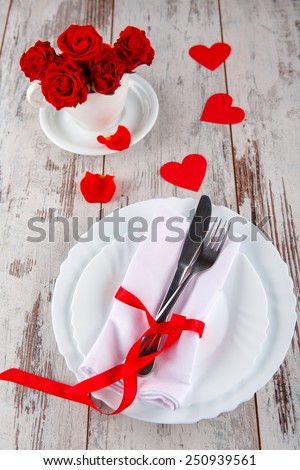The perfect valentines day. Closeup of wooden table served with romantic love decor and cutlery with roses in the cup