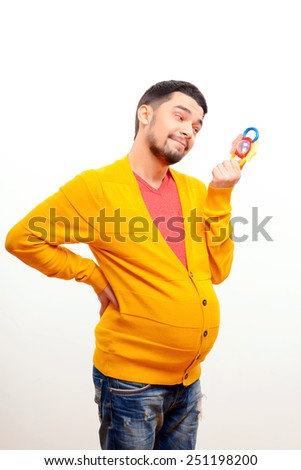 It is better to be prepared. Funny conceptual photo of gender reversal when a pregnant man with a belly holding a rattle toy while posing isolated on white background