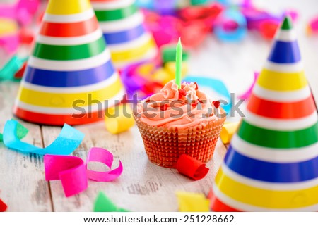 It is a special day. Image of a delicious cupcake with a candle surrounded by party hats and confetti on the background