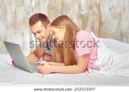 Beautiful young couple in bed. Handsome young man and woman lying in bed and watching something on laptop together