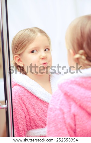 Pretty like my mother. Closeup image of a funny little girl in a pink bathrobe using face cream while standing in front of the big mirror