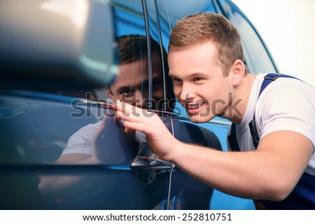 Welcome to our car service station. Closeup image of a smiling handsome car mechanic wiping the car in specialized service station