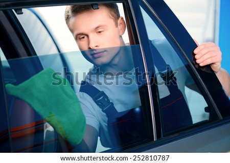 Welcome to our car service station. Closeup image of a handsome car mechanic wiping the car windows with tinting foil and smiling at camera in specialized service station