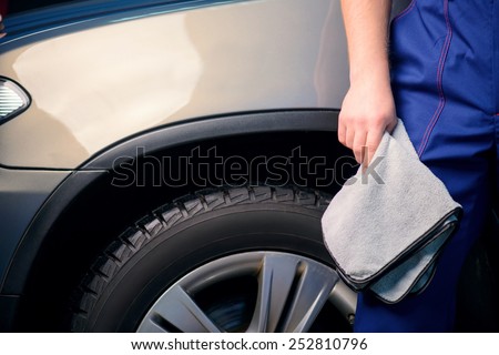 Welcome to our car service station. Closeup image of a handsome car mechanic in a uniform posing with a polishing wiper while standing against luxury suv in an authorized service station