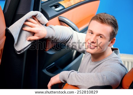 Cleaning his car. Top view of handsome smiling young man cleaning his car dash board with a wiper