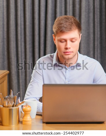 Having opportunity to work everywhere. Handsome young man working on laptop while sitting in city cafe on the curtain background with copy space